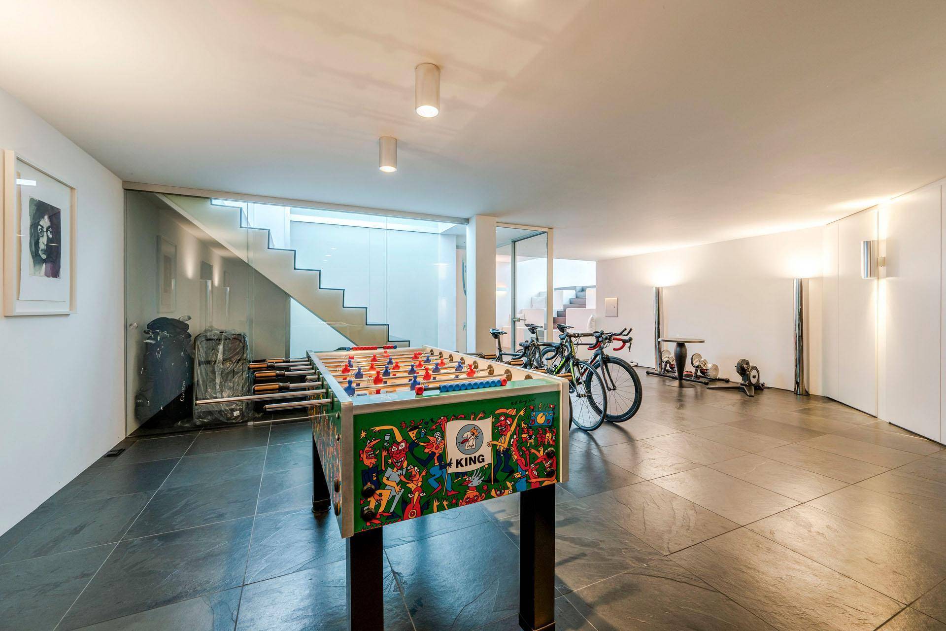 Geräumiger Freizeitraum mit Tischfußball, Fahrrädern und moderner Treppe im Hintergrund.