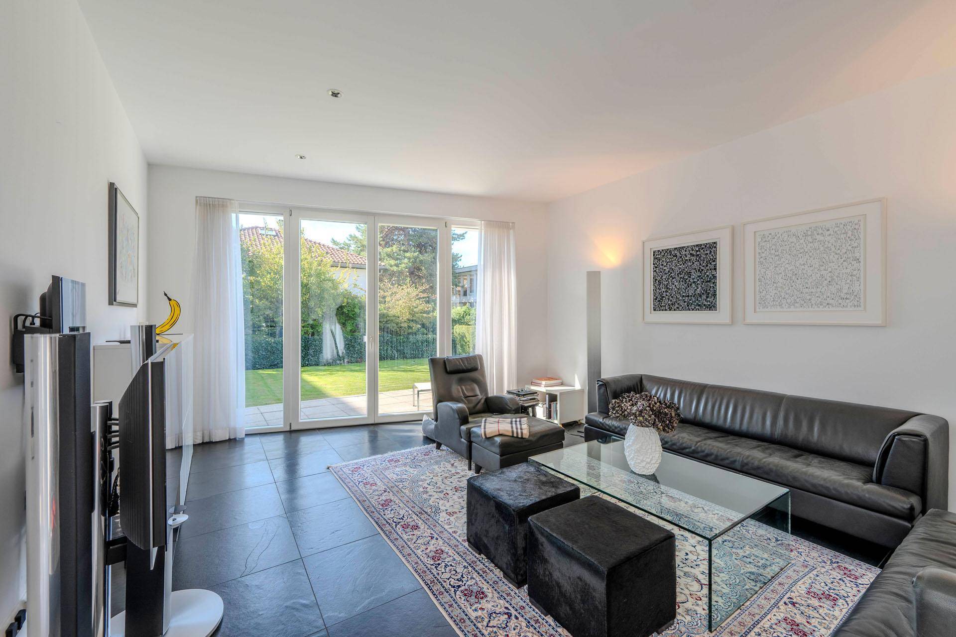 Gemütliches Wohnzimmer mit dunklem Ledersofa, Teppich und Zugang zum Garten.