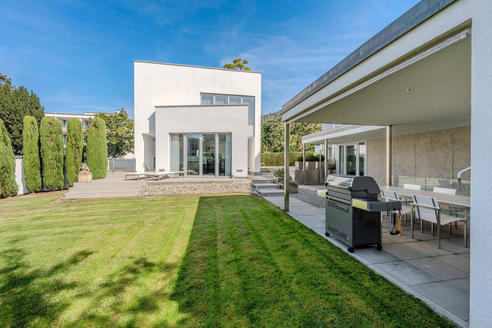 Gepflegter Gartenbereich mit Rasenfläche, Grillplatz und moderner Architektur im Hintergrund.