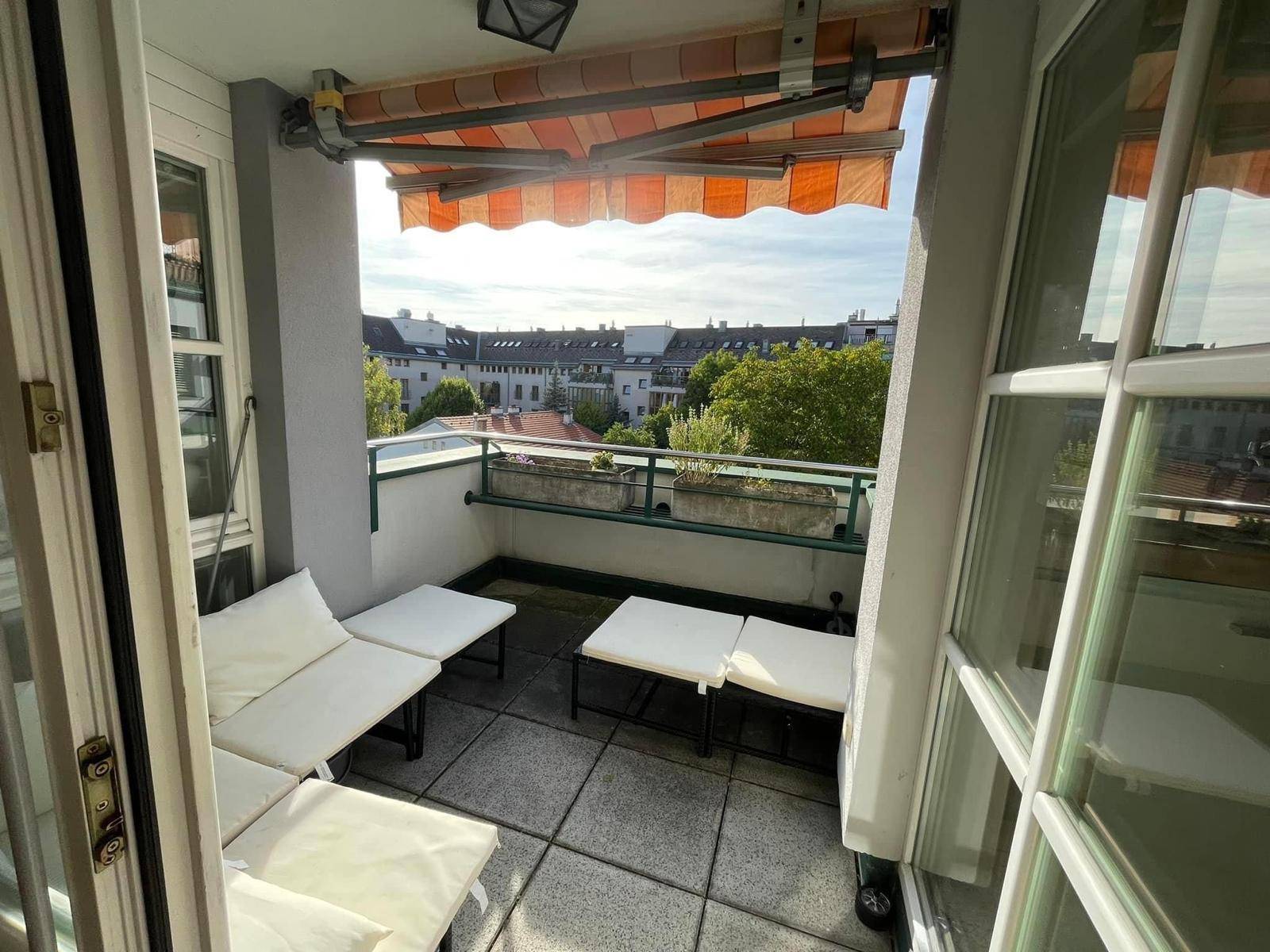 Gemütlicher Balkon mit Fliesenboden, Sitzgelegenheiten und Markise, bietet Blick auf die Umgebung.