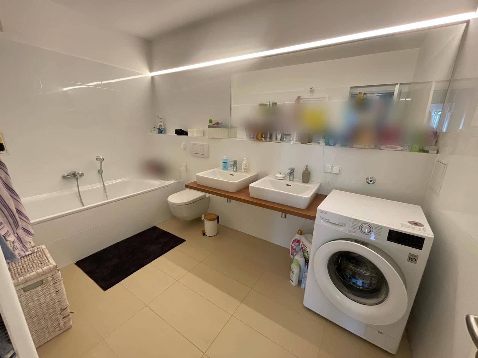 Modernes Badezimmer mit Badewanne, Doppelwaschbecken und Waschmaschine, hell gefliest.