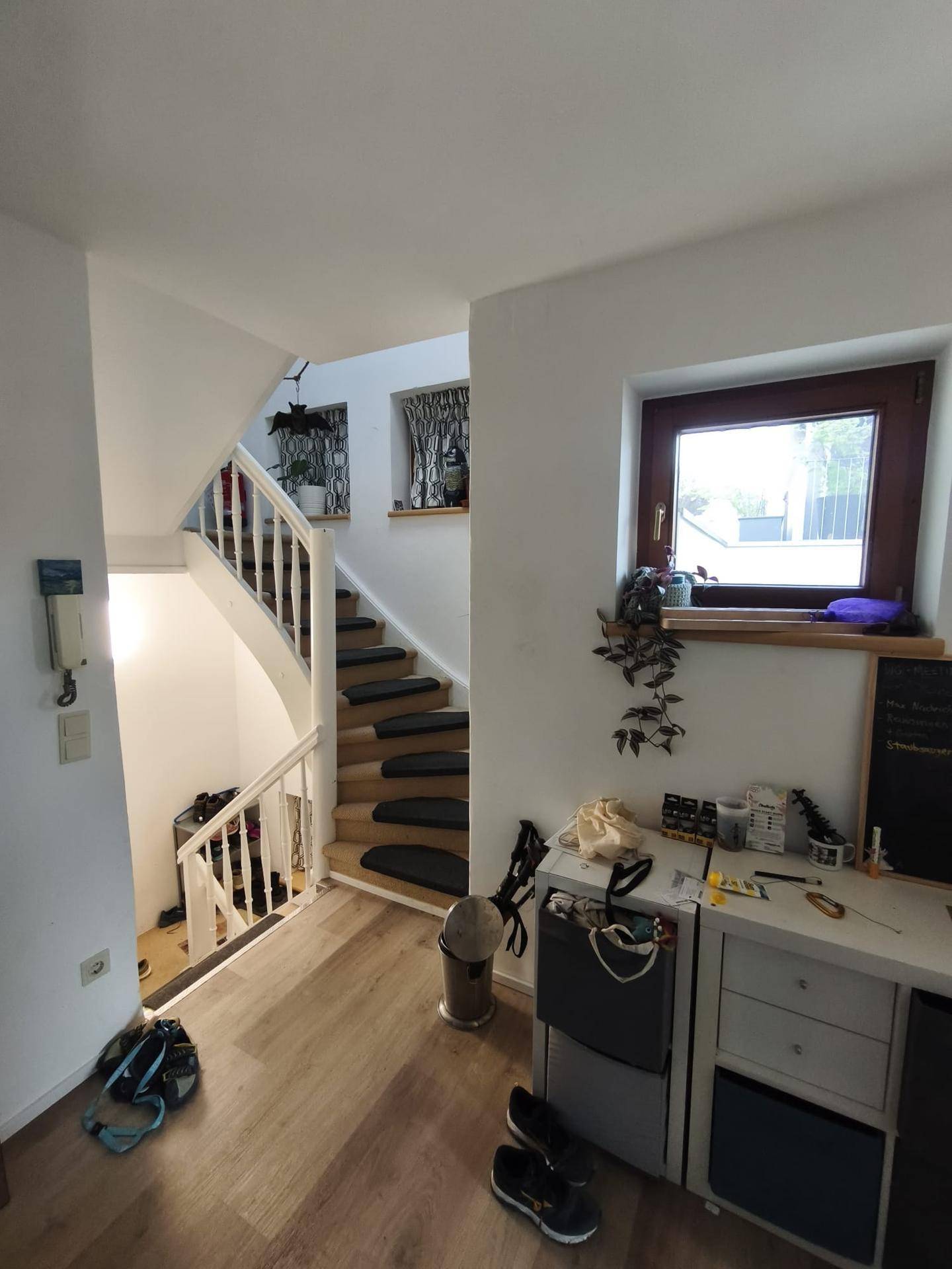Heller Flur mit Holztreppe, die in die oberen Stockwerke führt, und einem kleinen Arbeitsbereich.