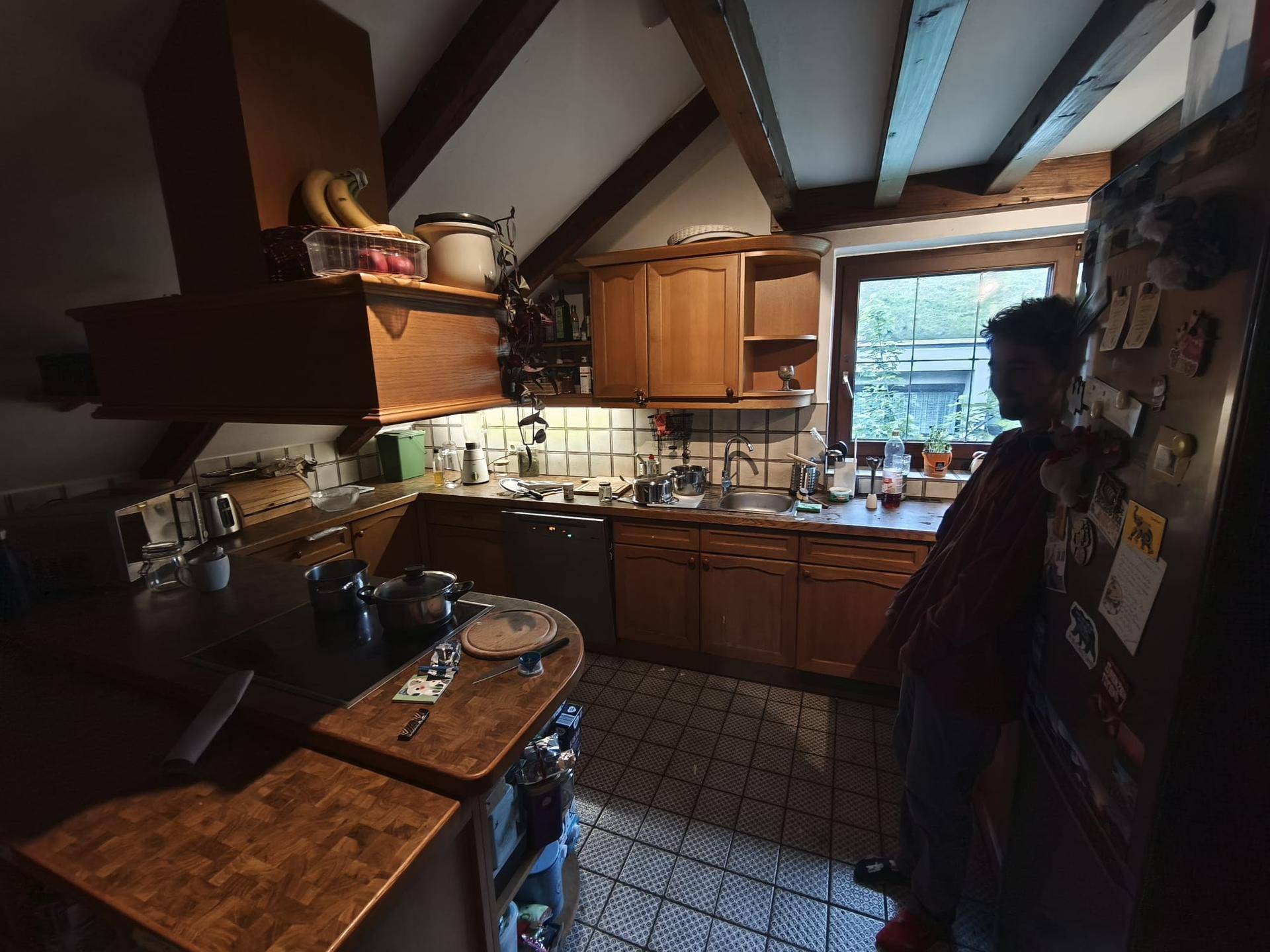 Rustikale Küche im Dachgeschoss mit Holzschränken, Fliesenboden und sichtbaren Deckenbalken.