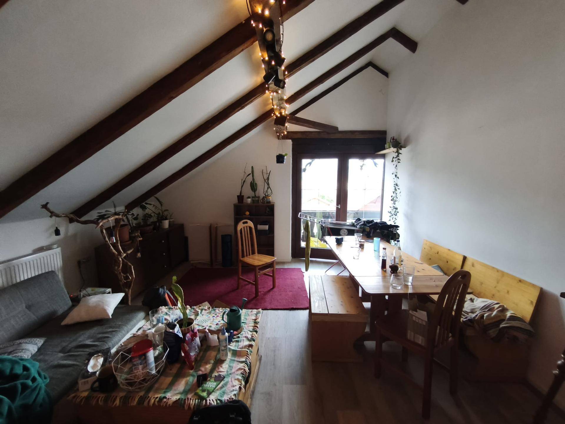 Gemütlicher Wohn-Essbereich im Dachgeschoss mit sichtbaren Holzbalken und Zugang zum Balkon.