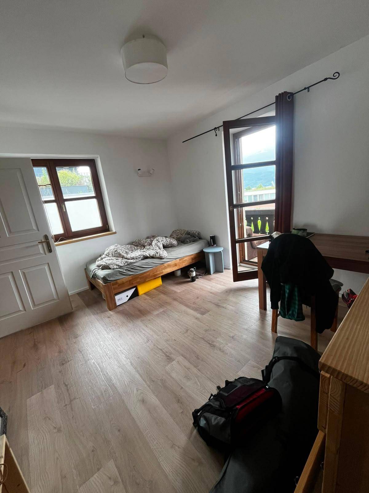 Helles Schlafzimmer mit Holzbett, Laminatboden und Fenster sowie Balkonzugang.