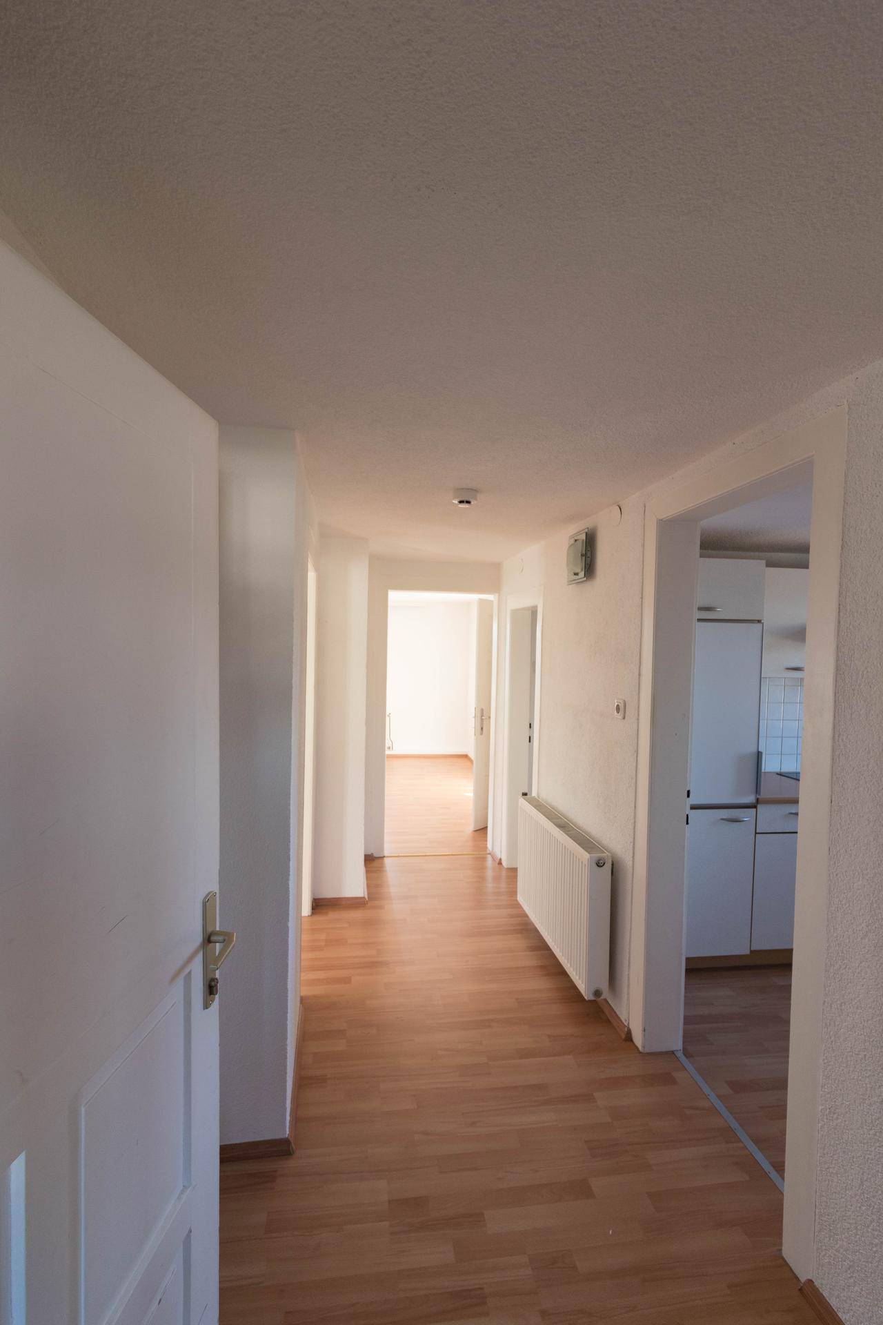 Heller Flur mit Laminatboden und Zugang zu verschiedenen Räumen, inklusive Blick in die Küche.