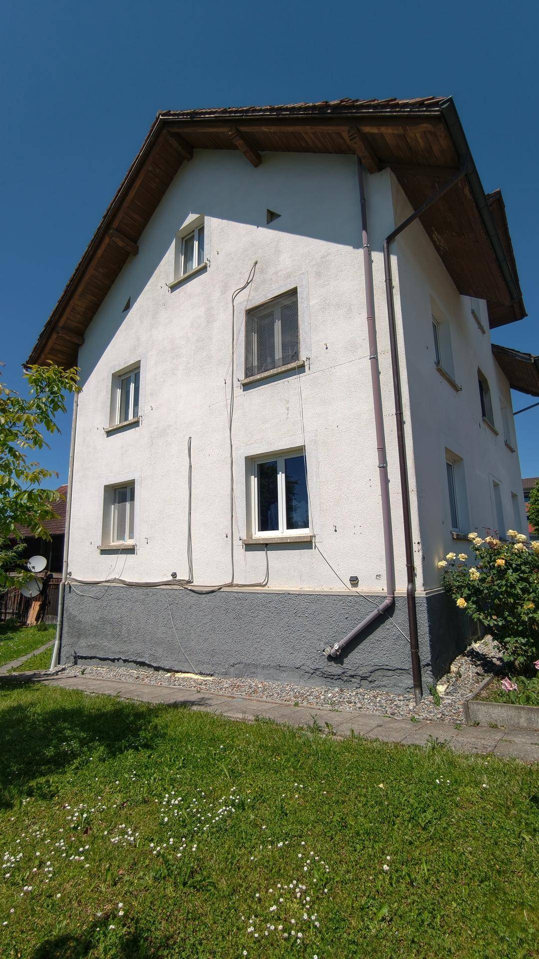 Seitenansicht des weißen Mehrfamilienhauses mit Fenstern und einem gepflegten Rasenbereich.