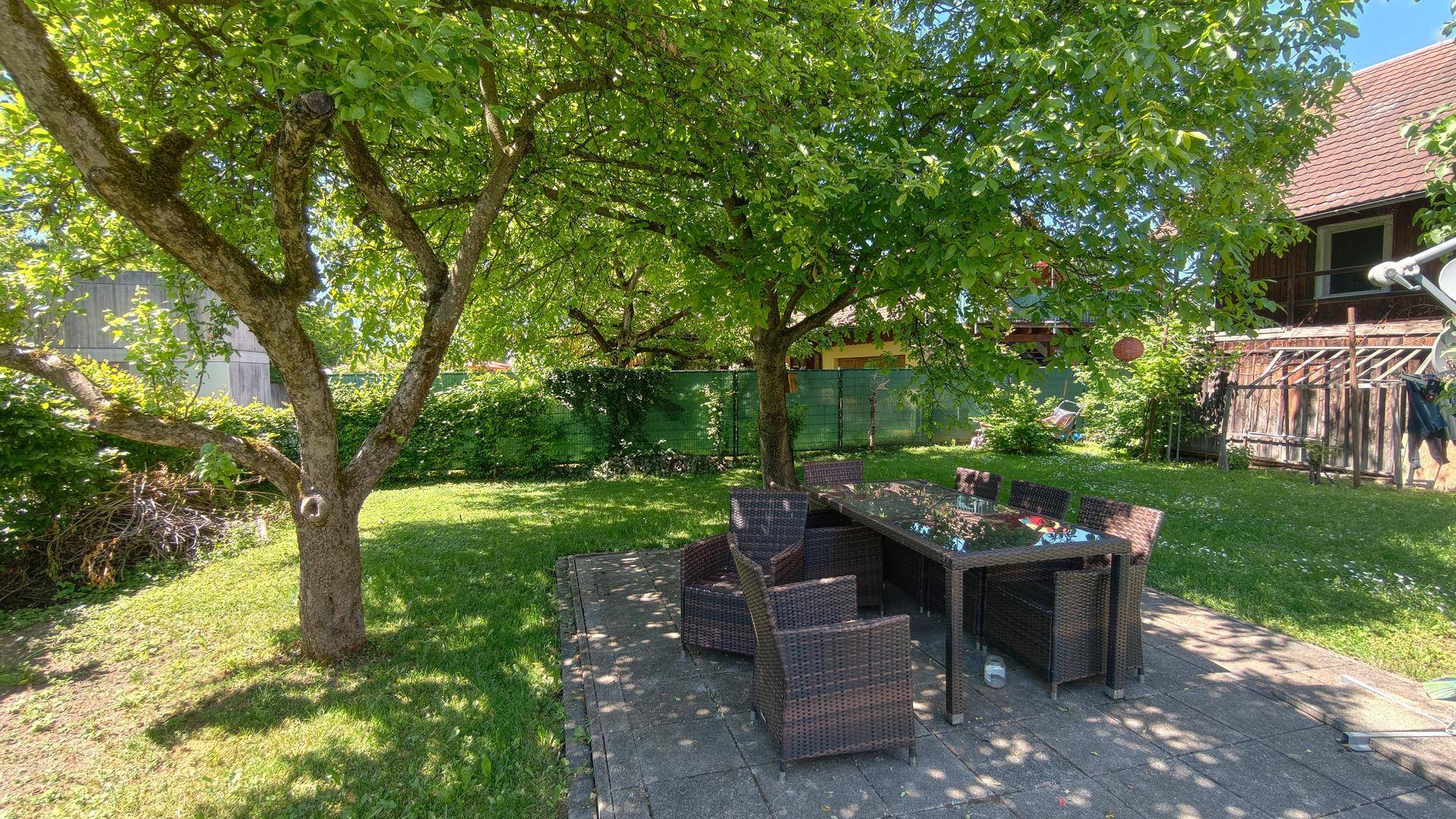 Gemütlicher Gartenbereich mit schattenspendenden Bäumen und einer möblierten Terrasse.