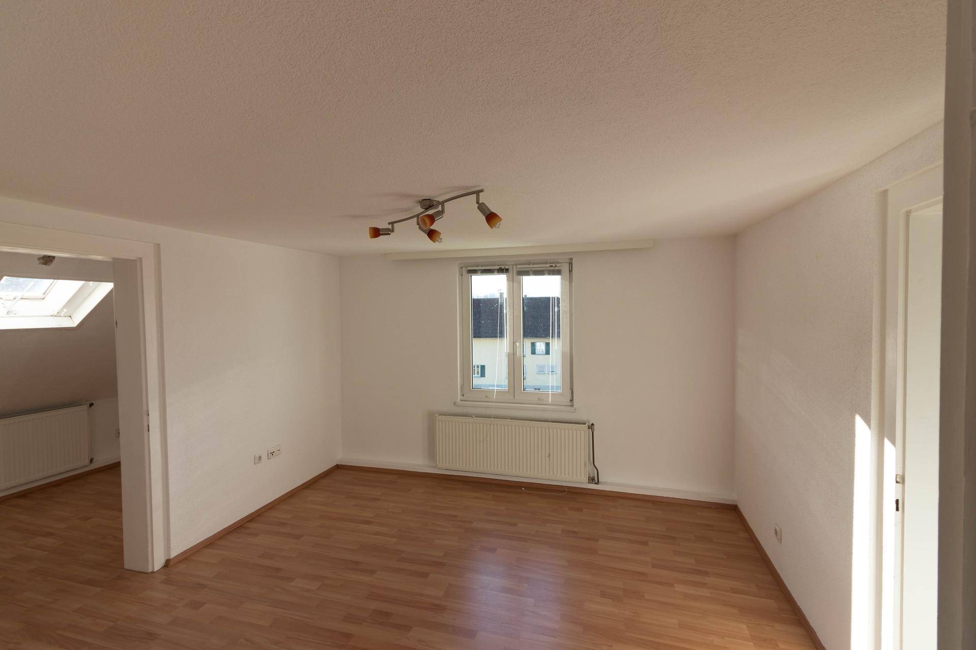 Geräumiges Zimmer mit Laminatboden, Fenster und Zugang zu einem weiteren Raum mit Dachfenster.