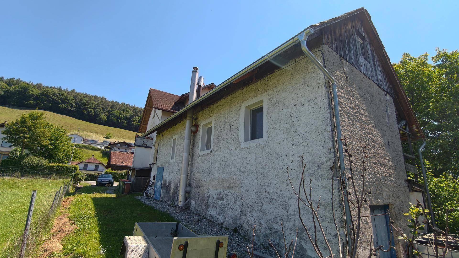 Seitenansicht des Gebäudes mit Anbau und Blick auf eine grüne Hügellandschaft.