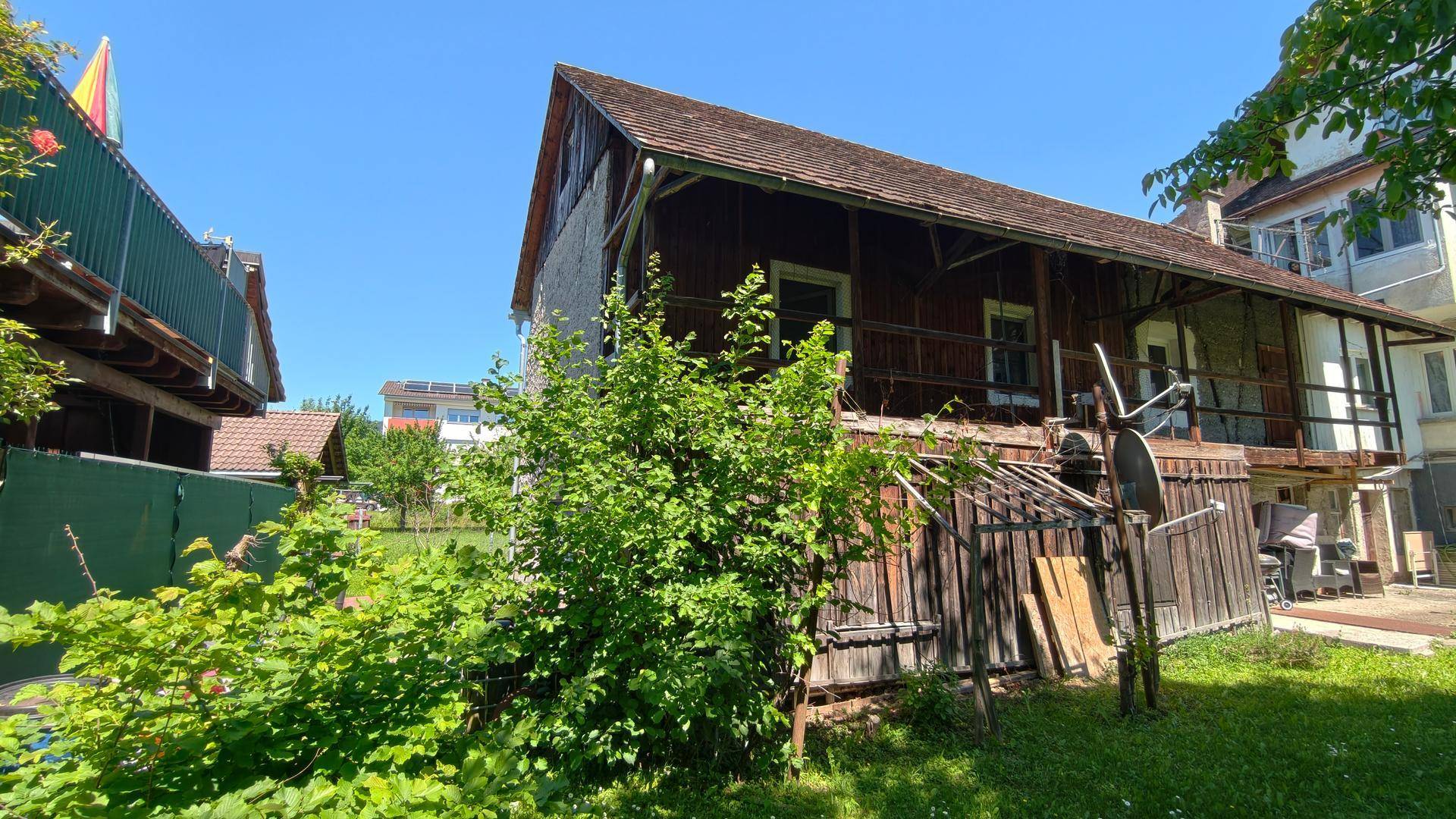 Rustikales Nebengebäude mit Holzbalkonen und üppiger Vegetation im Gartenbereich.