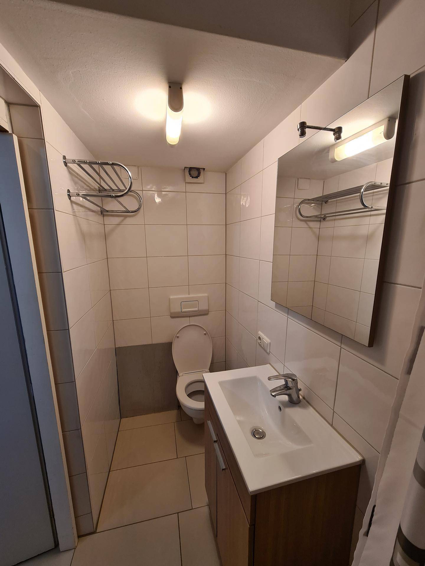 Kleines WC mit Waschbecken, Spiegel und weißen Wandfliesen.