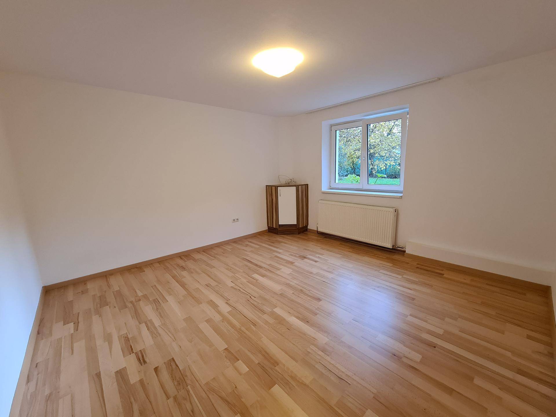 Helles Schlafzimmer mit Holzboden, Fenster und Blick ins Grüne.