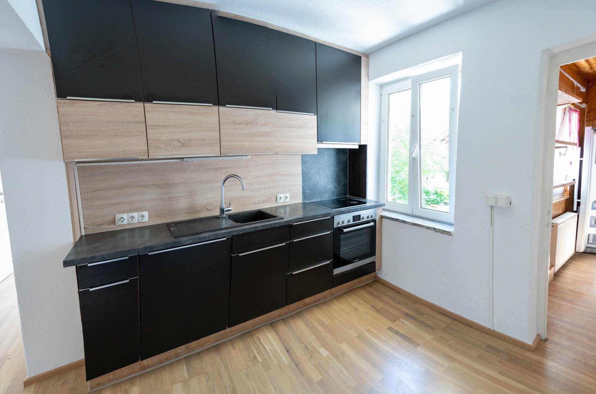 Moderne Küche mit schwarzen und holzfarbenen Schränken, Fenster und Holzboden.
