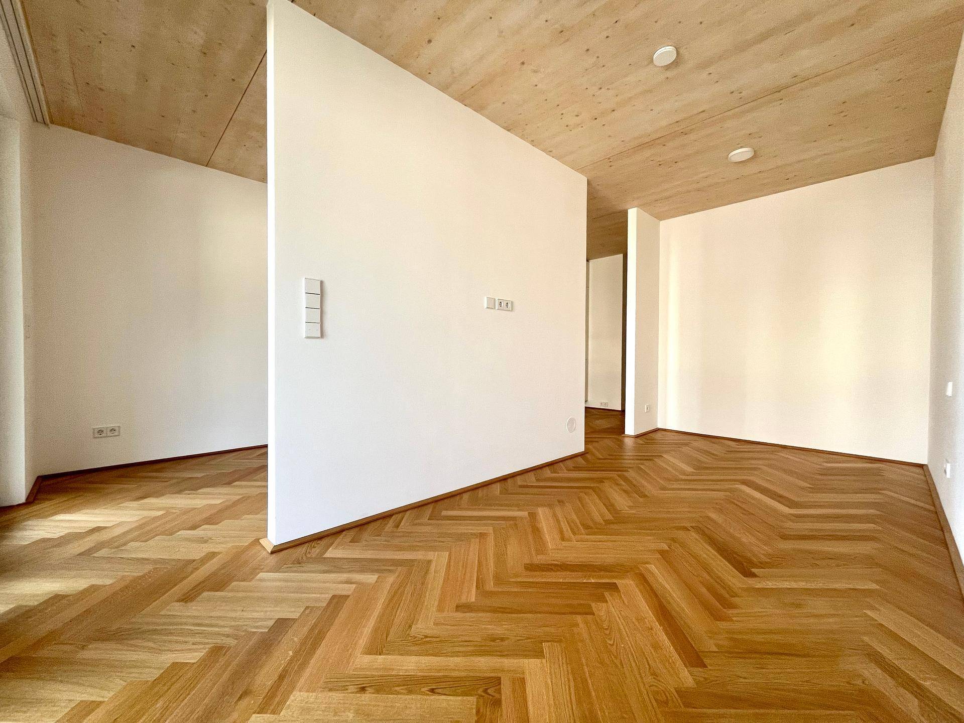 Geräumiger offener Wohnbereich mit Fischgrätparkettboden und einer charakteristischen Holzbalkendecke.