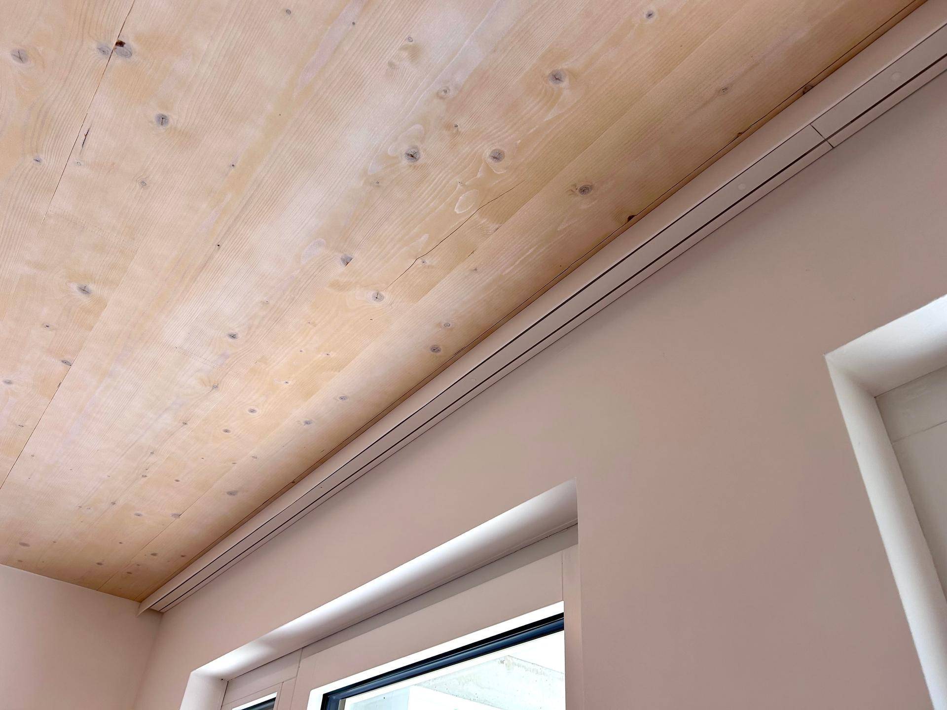 Detailaufnahme einer modernen Holzbalkendecke mit integrierter Beleuchtung und weißer Wand.