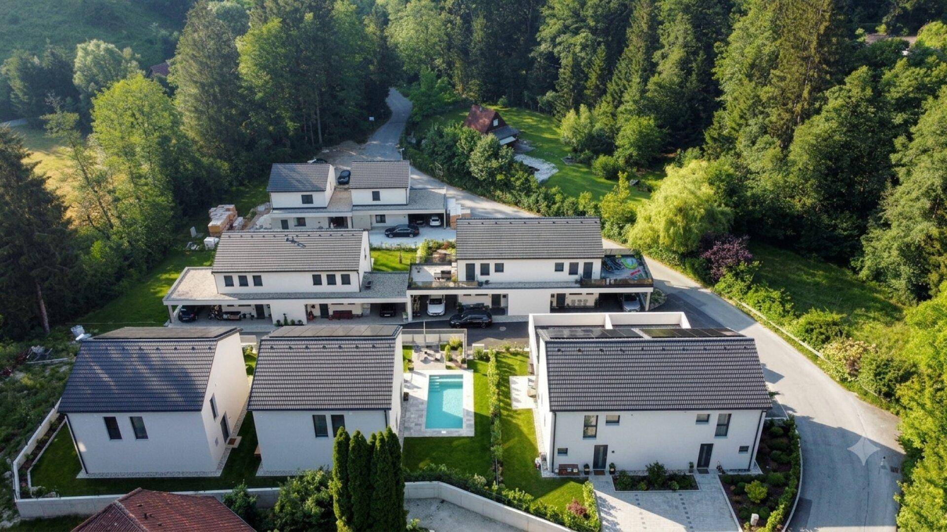 Panoramablick auf eine moderne Wohnanlage, umgeben von viel Grün und Wald.