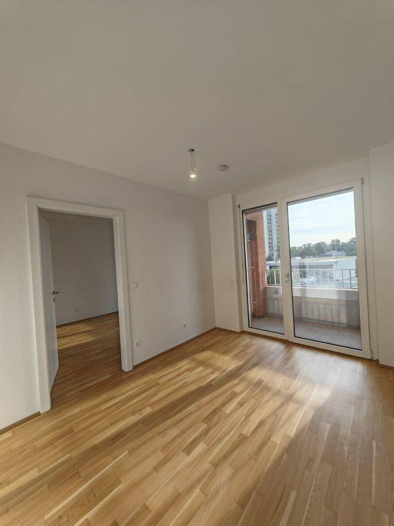 Helles Zimmer mit Holzboden und Zugang zu einem Balkon, ideal als Schlaf- oder Wohnraum.