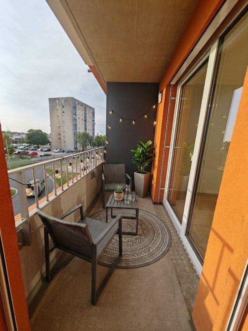 Möblierter Balkon mit Sitzgelegenheiten, Pflanzen und Lichterkette, bietet einen Stadtblick.