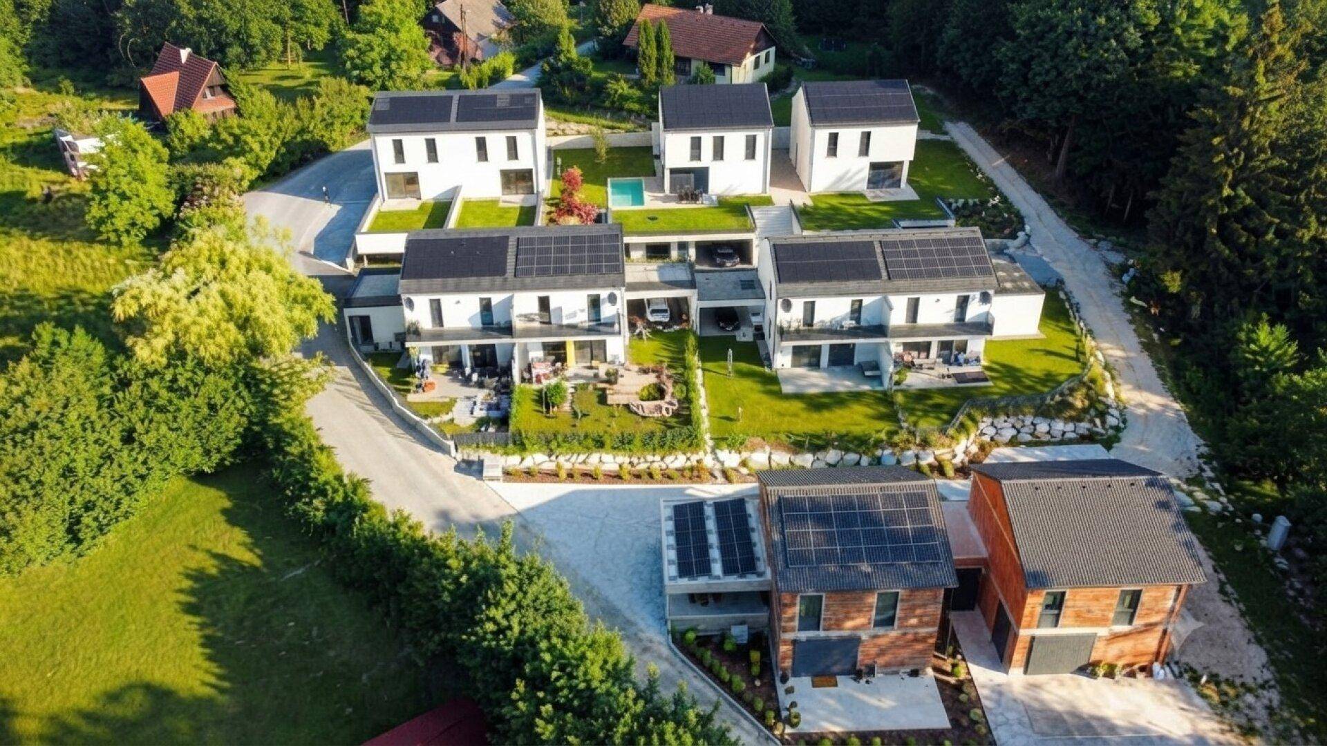 Luftaufnahme einer modernen Wohnsiedlung mit mehreren Häusern, Photovoltaikanlagen und viel Grün.