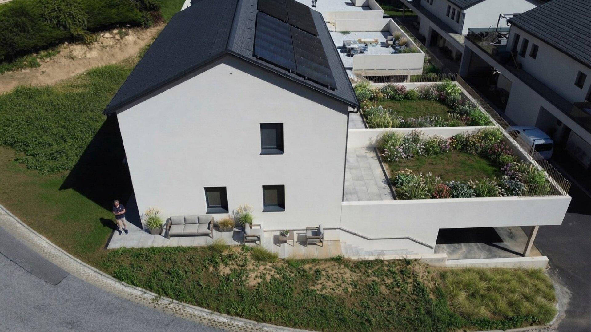 Modernes Haus mit begrüntem Dach, Terrasse und integriertem Carport, umgeben von natürlicher Landschaft.
