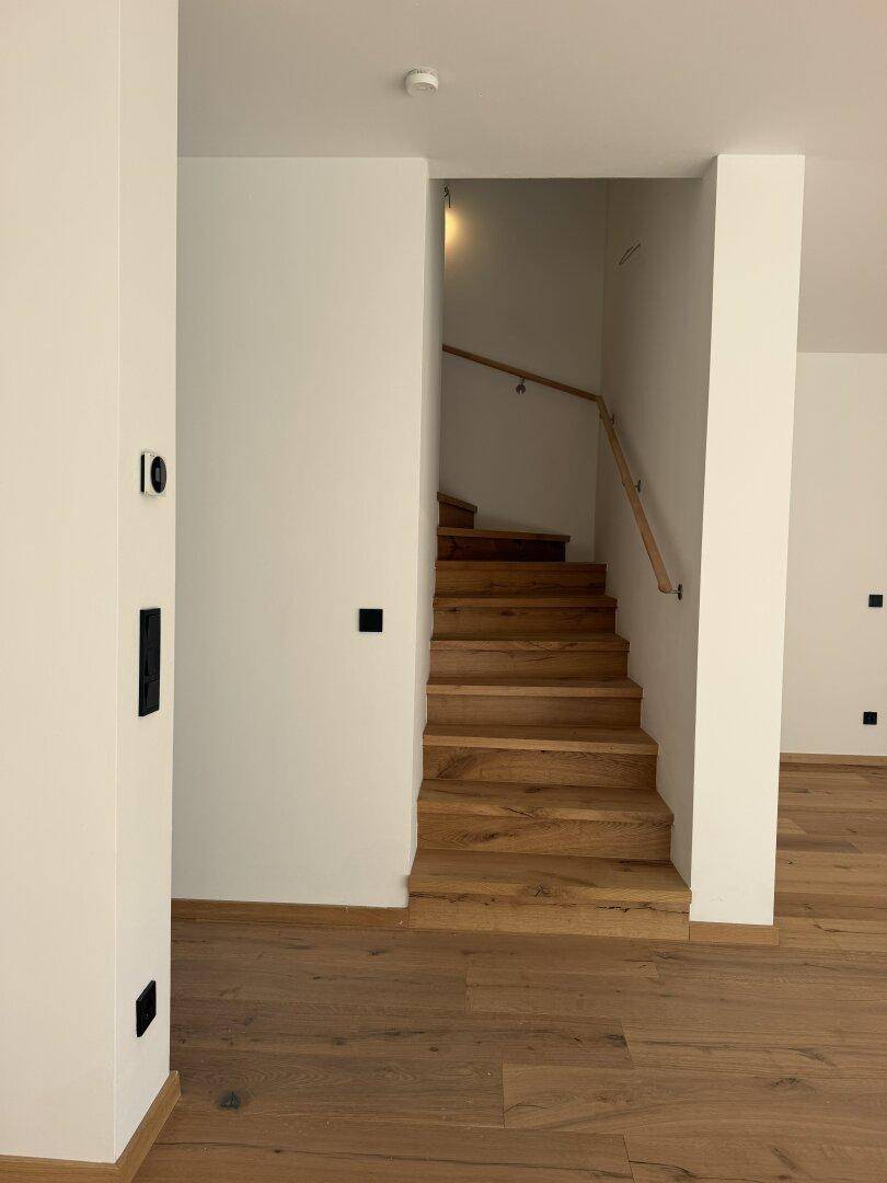 Heller Eingangsbereich mit Eichenparkettboden und einer Holztreppe mit schlichtem Geländer.