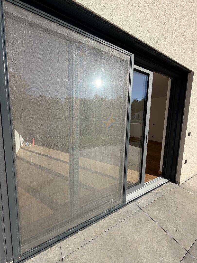 Große Glasschiebetür mit Insektenschutz, die den Zugang zu einer modernen Terrasse ermöglicht.