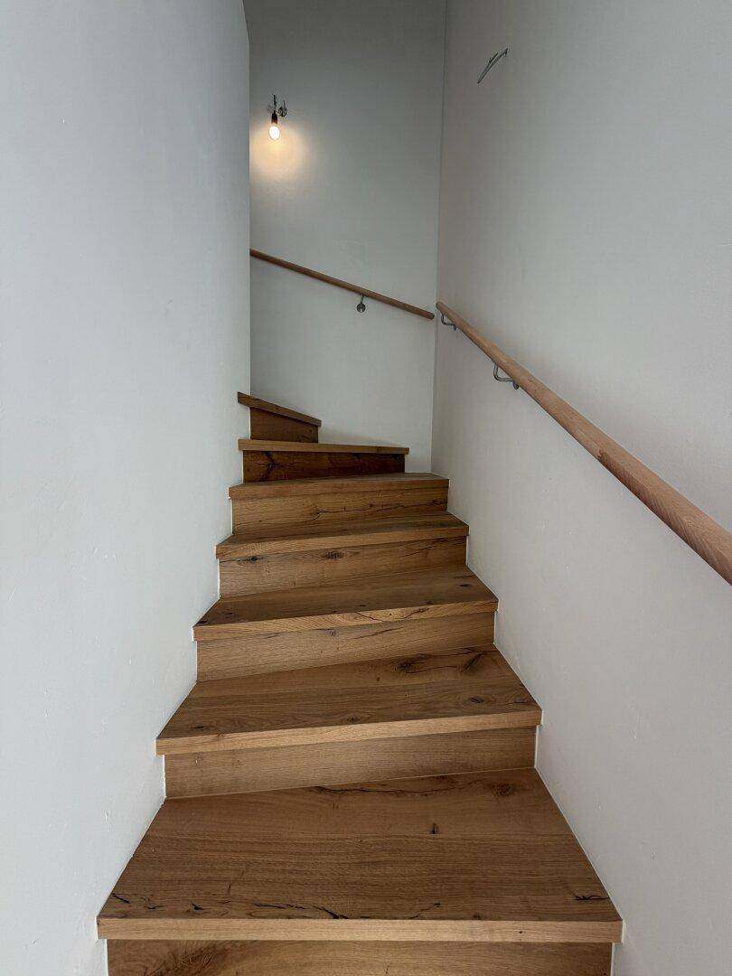 Elegante Holztreppe mit Eichenstufen und schlichtem Holzgeländer in einem hellen Treppenhaus.