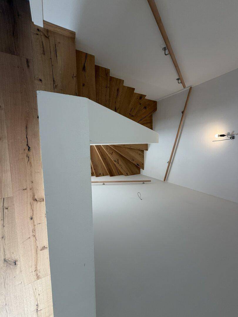 Blick von oben auf eine geschwungene Holztreppe mit Eichenstufen und weiß gestrichenen Wänden.