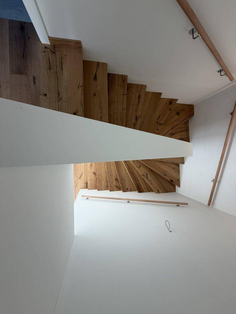Geschwungene Holztreppe mit Eichenstufen und minimalistischem Design, die die verschiedenen Ebenen verbindet.