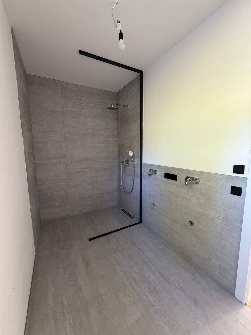 Geräumige, moderne Dusche mit grauen Fliesen und minimalistischem Design in einem neuen Badezimmer.