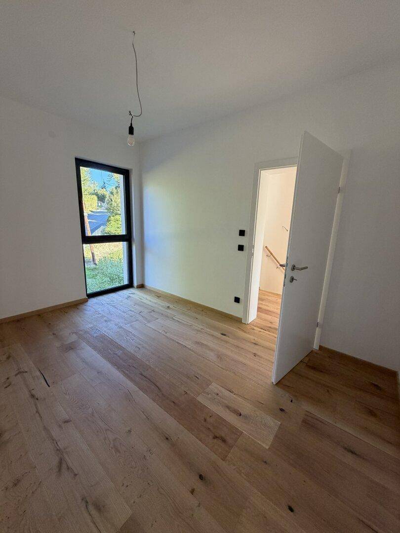 Helles Schlafzimmer mit Eichenparkettboden, großem Fenster und Zugang zu einem weiteren Raum.