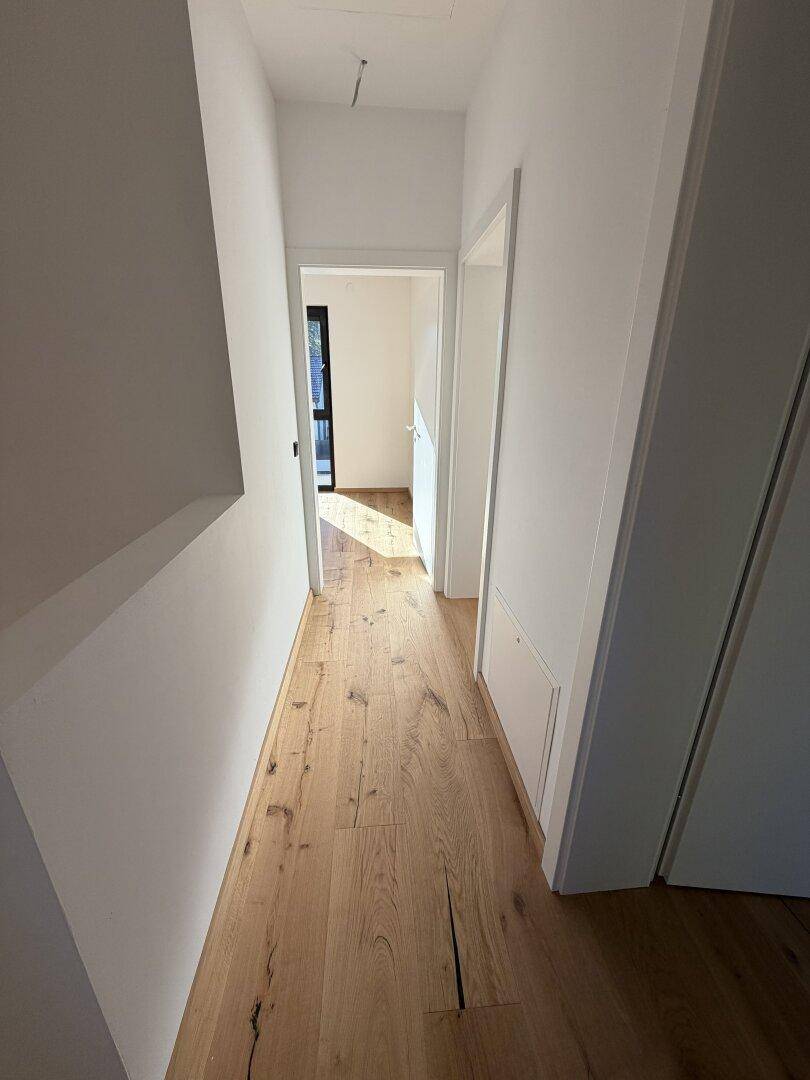 Heller Flur mit Holzdielenboden und weißen Wänden, der zu weiteren Räumen führt.