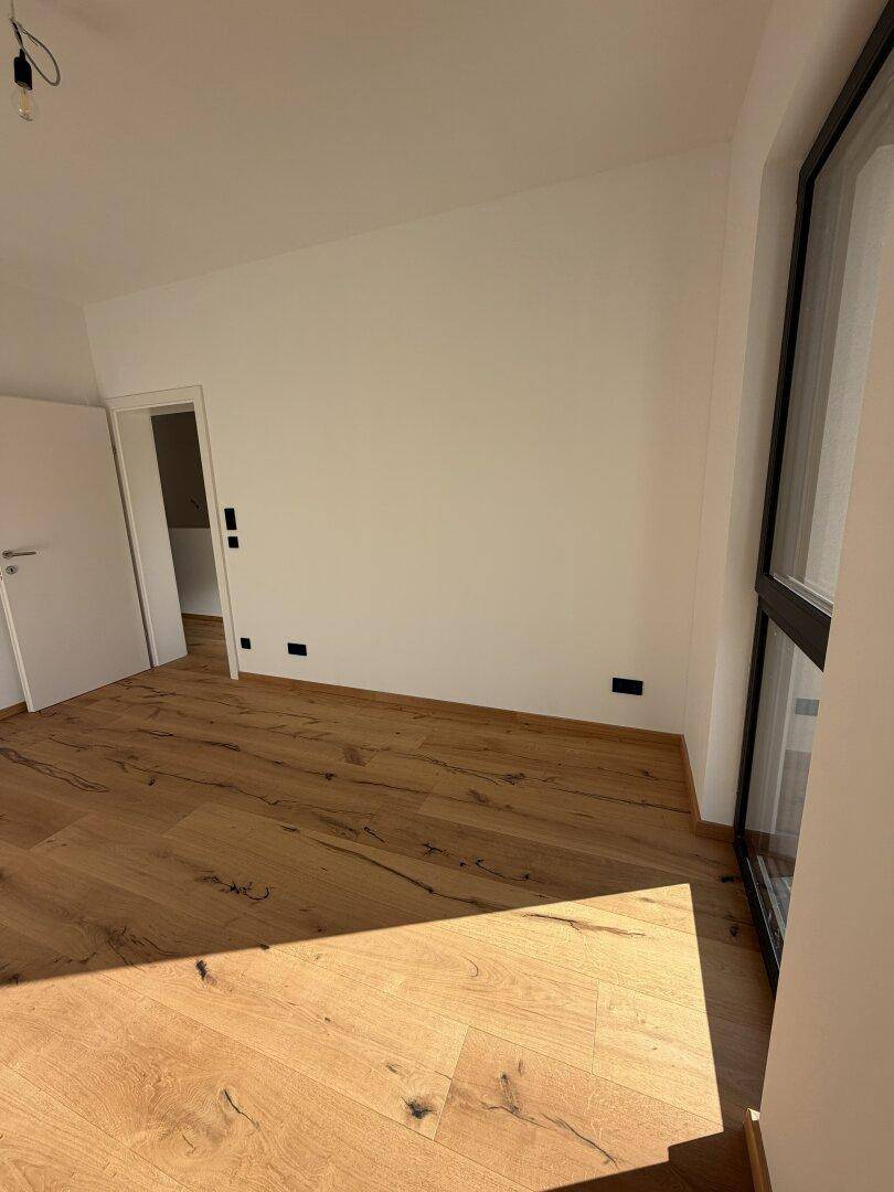 Sonniger Raum mit Holzdielenboden und bodentiefen Fenstern, die viel Tageslicht hereinlassen.
