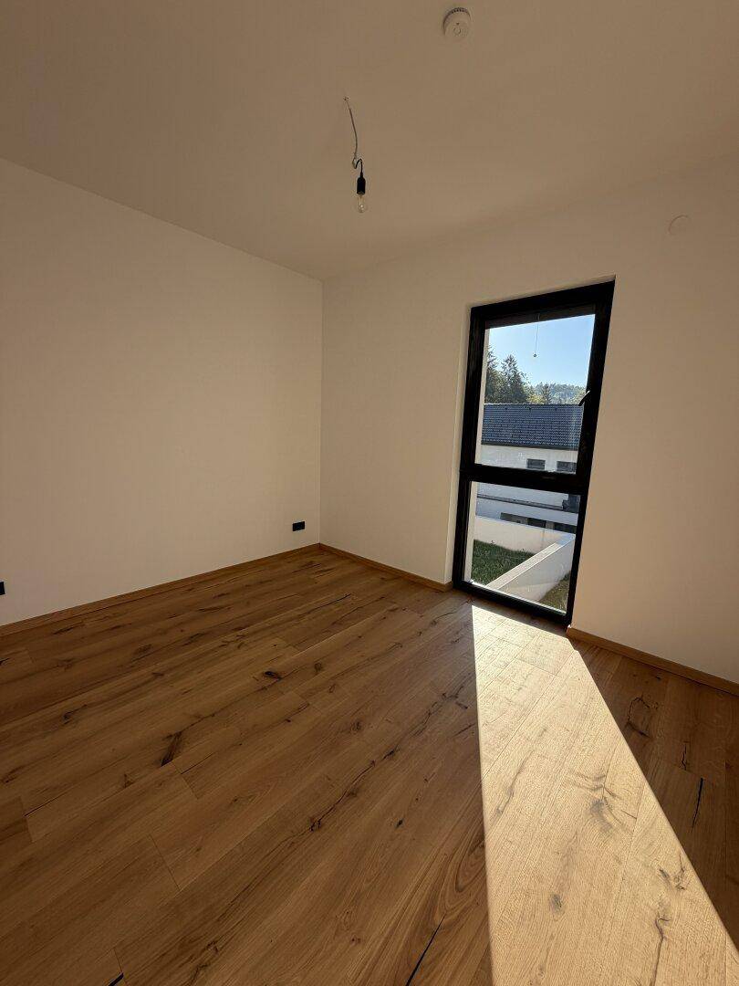 Heller Raum mit Holzdielenboden und Fenster, das einen Blick auf die umliegenden Häuser bietet.