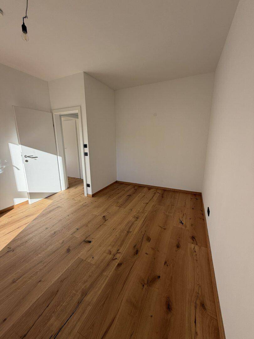Geräumiger, heller Raum mit Holzdielenboden und Zugang zu einem angrenzenden Flur.