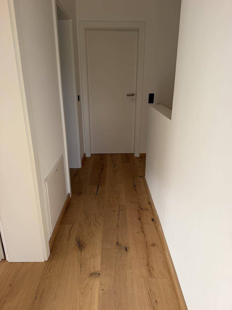 Schlichter Flur mit Holzdielenboden und weißen Türen, der verschiedene Wohnbereiche verbindet.
