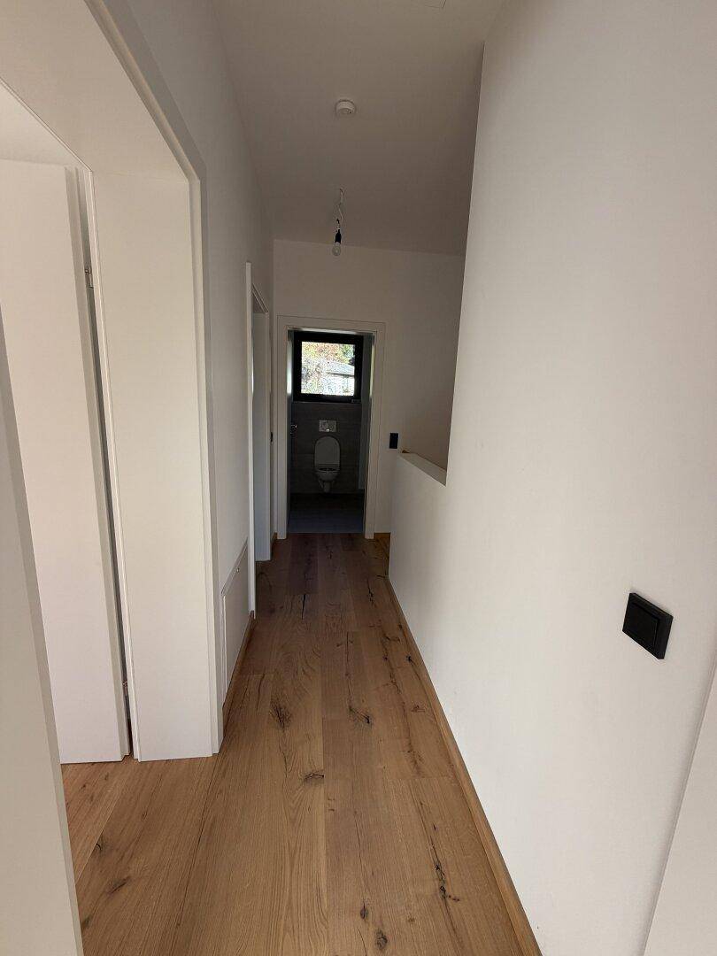 Langer Flur mit Holzdielenboden und Blick in ein separates Gäste-WC am Ende.