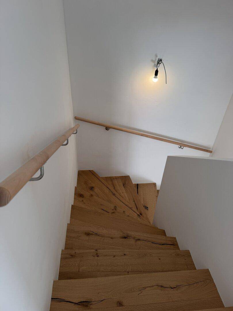 Moderne Holztreppe mit passendem Holzgeländer und weißen Wänden, die die Etagen verbindet.