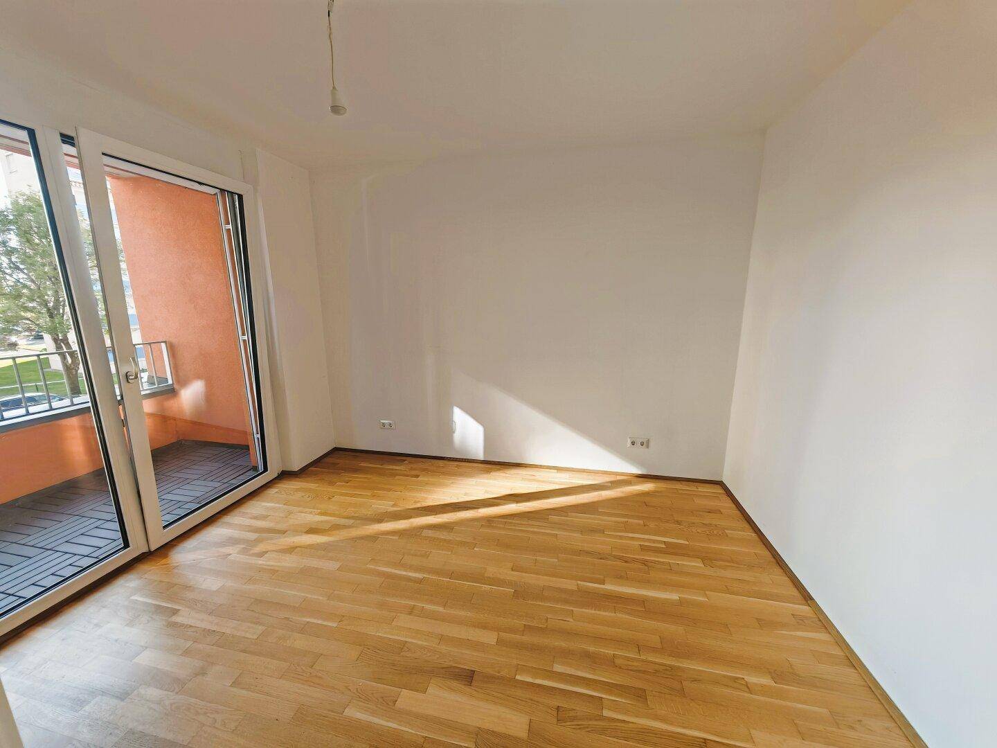 Lichtdurchflutetes Zimmer mit Holzboden und großem Schiebetürzugang zum Balkon.