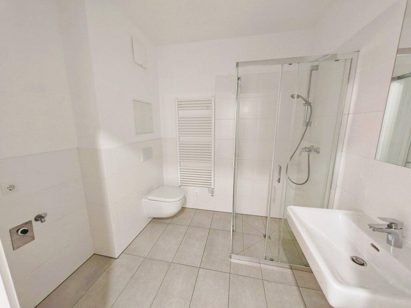 Modernes Badezimmer mit Duschkabine, wandhängendem WC und beheiztem Handtuchhalter.
