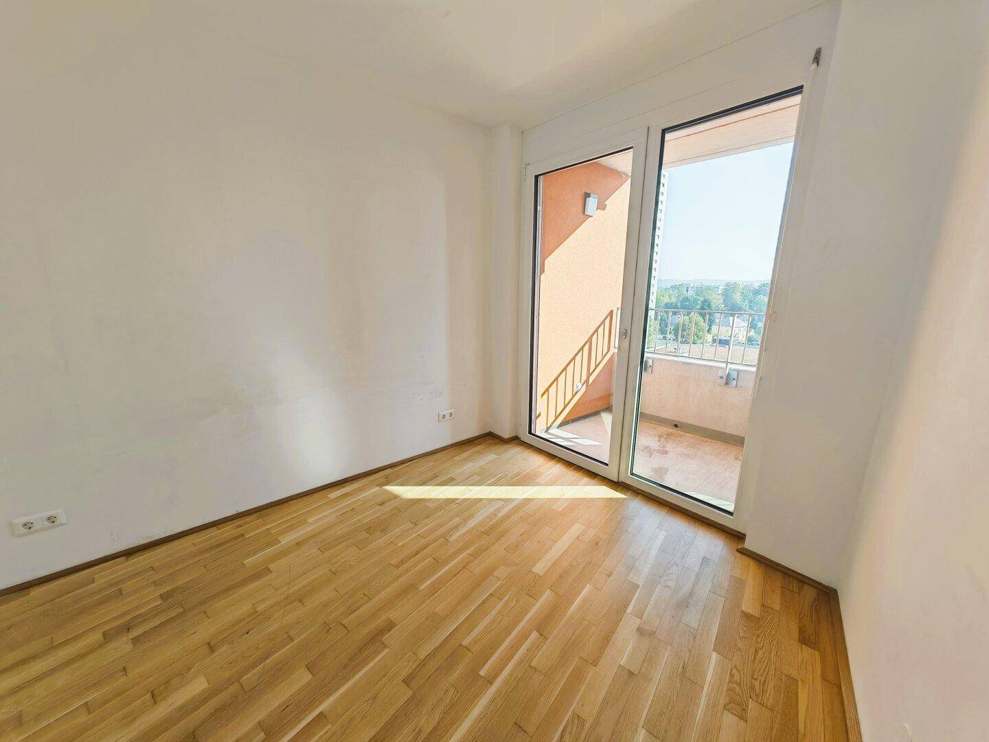 Lichtdurchflutetes Zimmer mit Parkettboden und direktem Zugang zu einem Balkon.