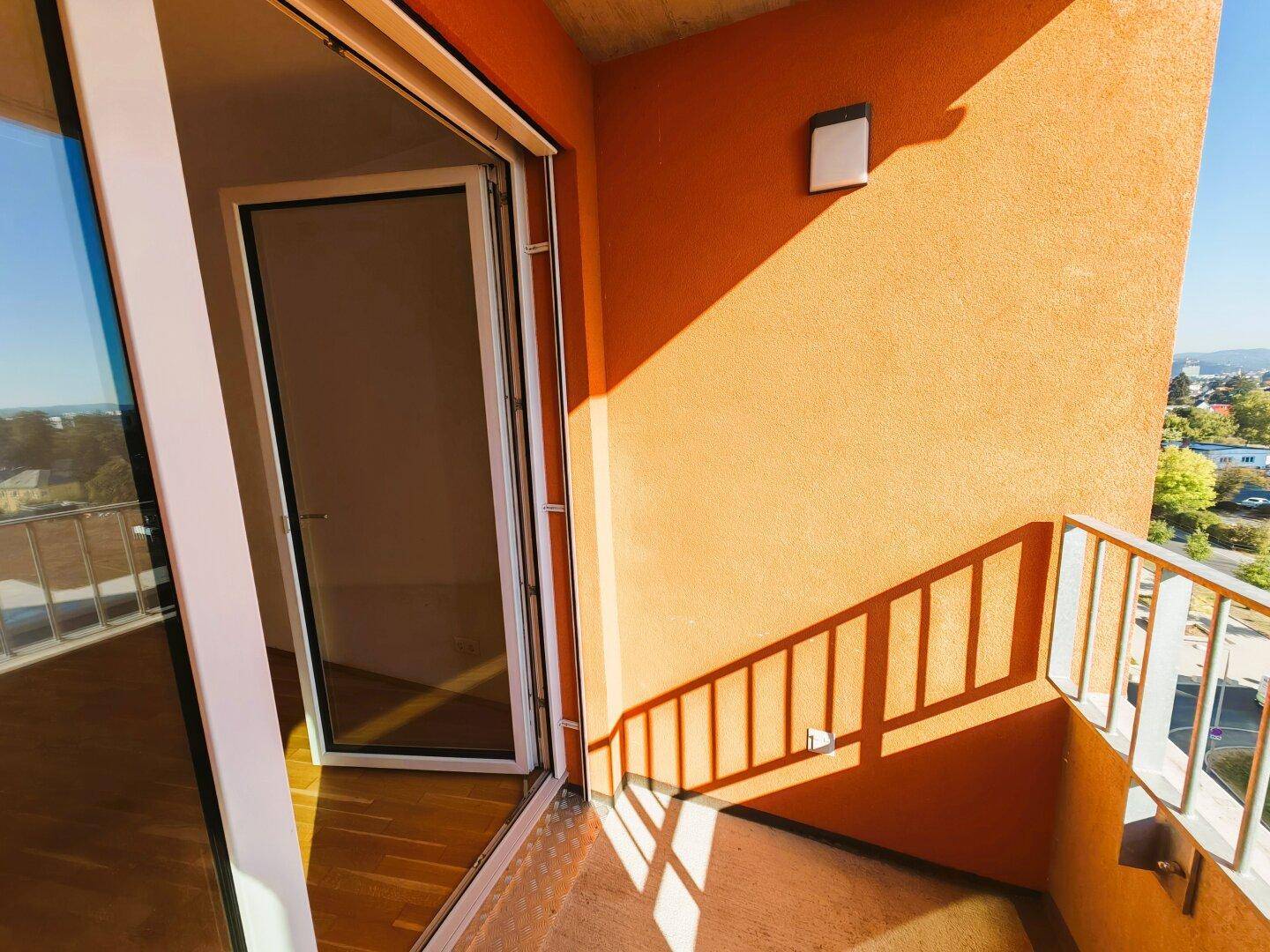 Sonniger Balkon mit orangefarbener Fassade und Blick auf die Umgebung.