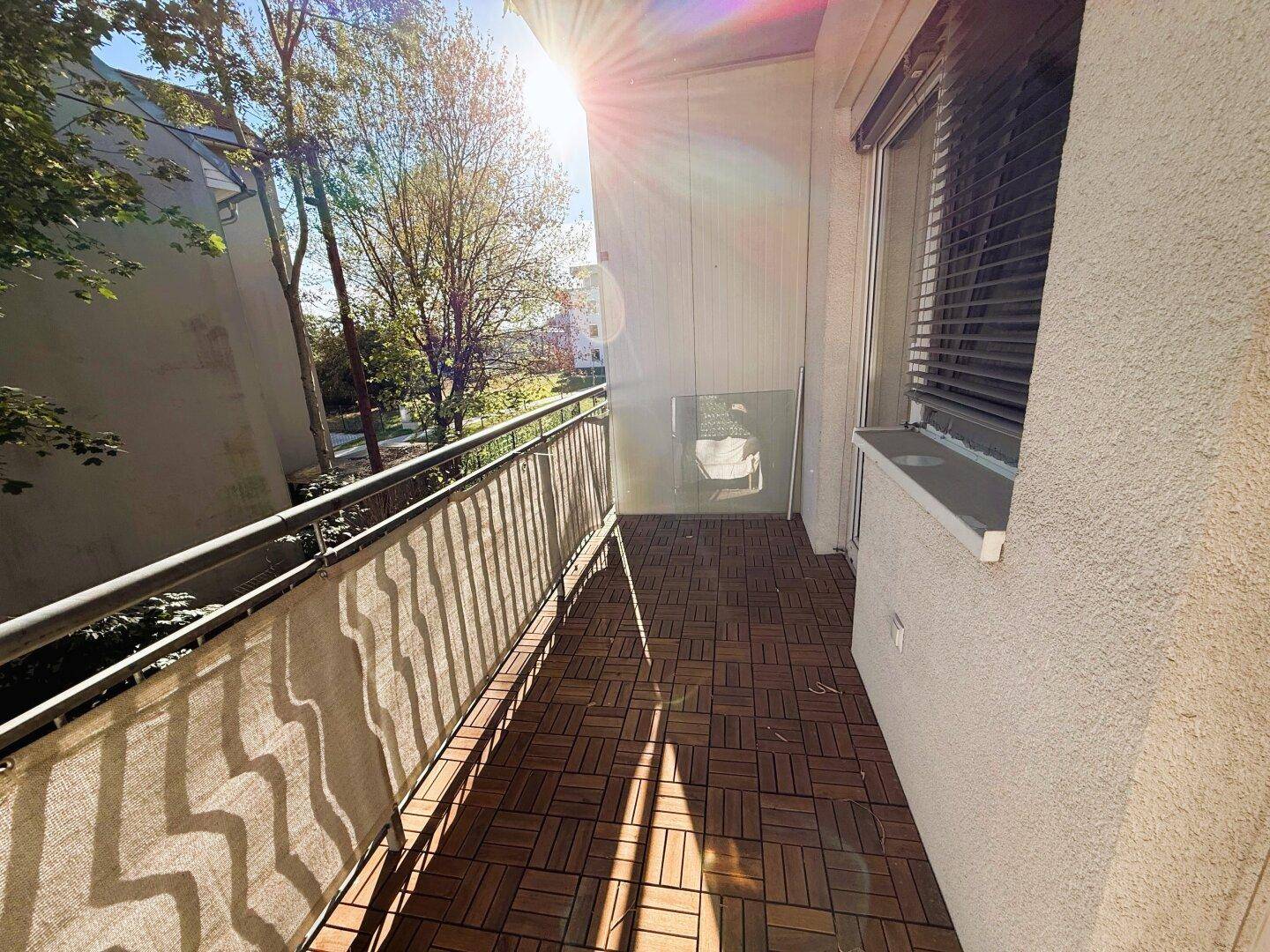 Sonniger Balkon mit Holzdielen und Metallgeländer, bietet einen angenehmen Außenbereich.