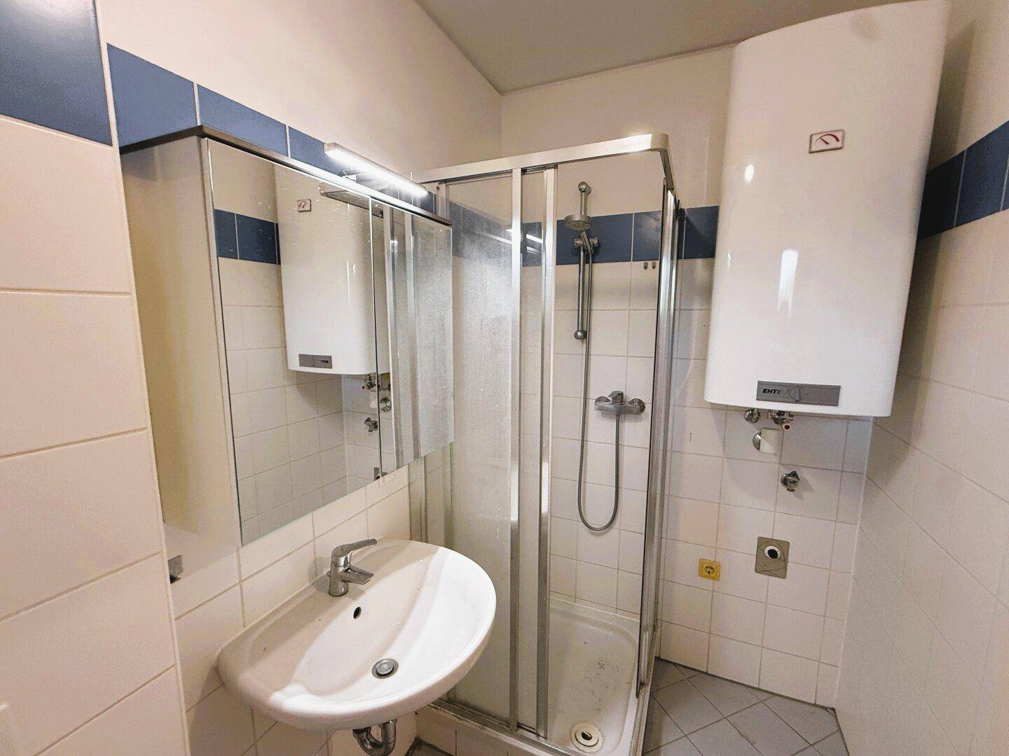 Funktionales Badezimmer mit Dusche, Waschbecken und Wandspiegel, in gutem Zustand.