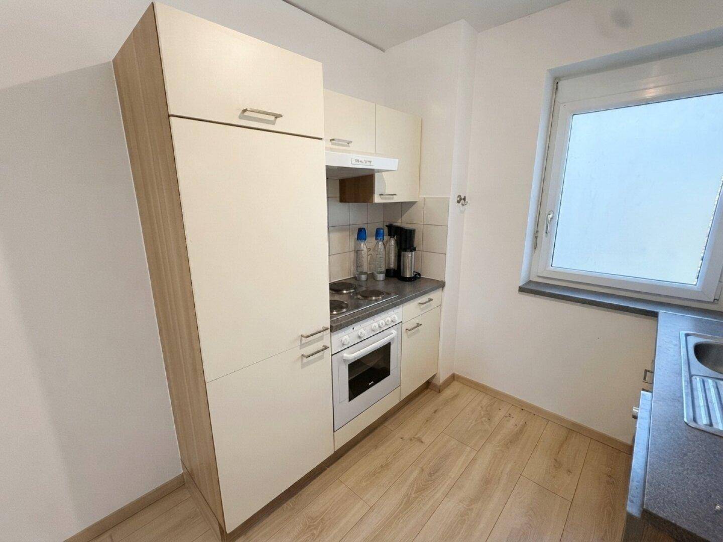 Kleine, funktionale Küchenzeile mit Herd, Backofen und Oberschränken, ideal für Singles.