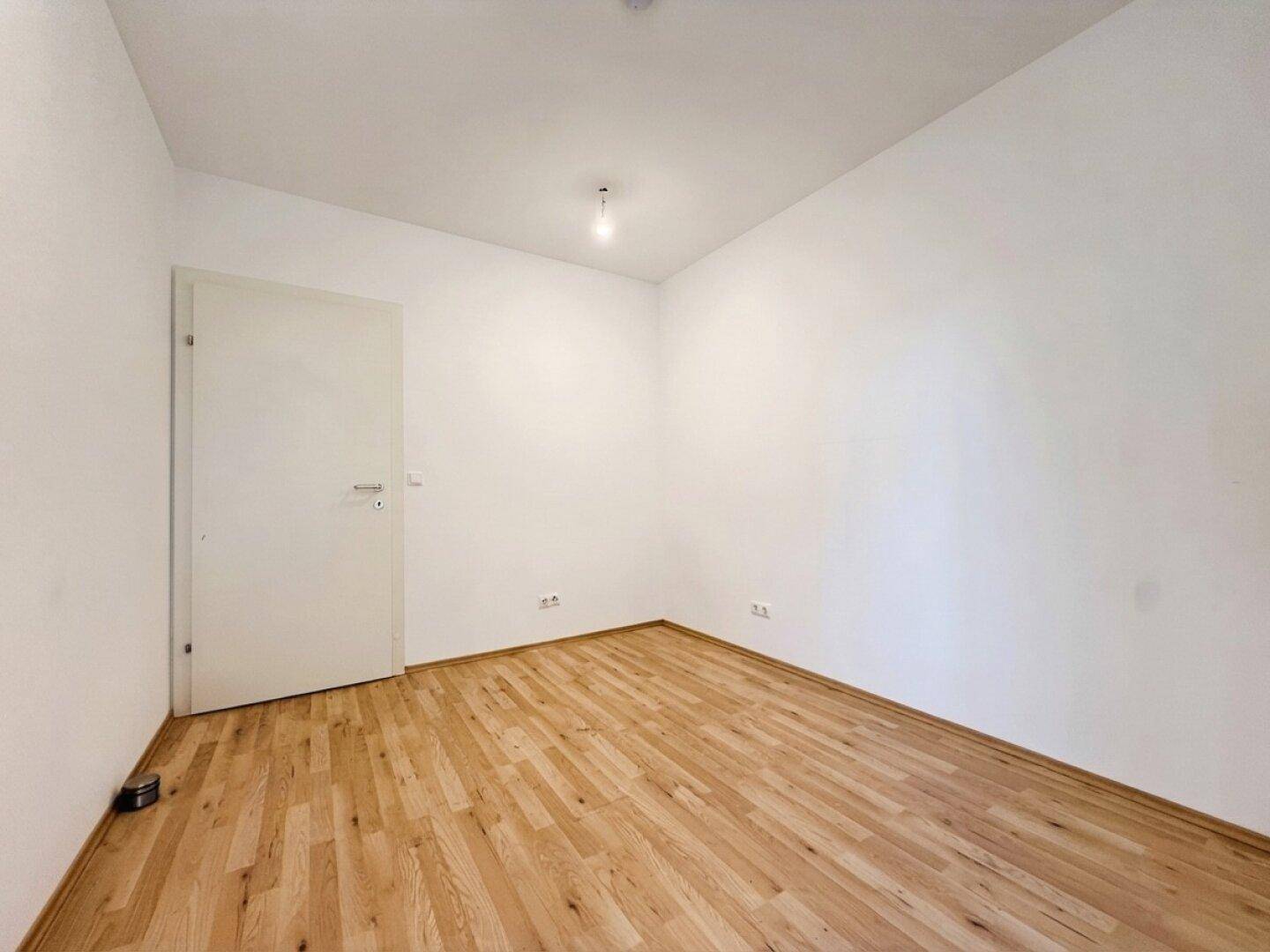 Schlichtes, leeres Zimmer mit Holzboden und weißer Tür, bereit zur individuellen Gestaltung.