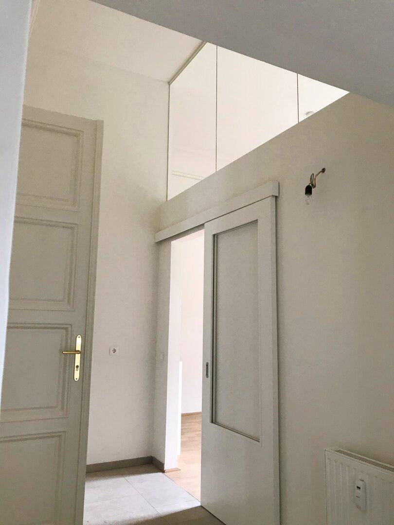 Heller Flur mit hohen Decken und einer modernen Schiebetür zu weiteren Räumen.