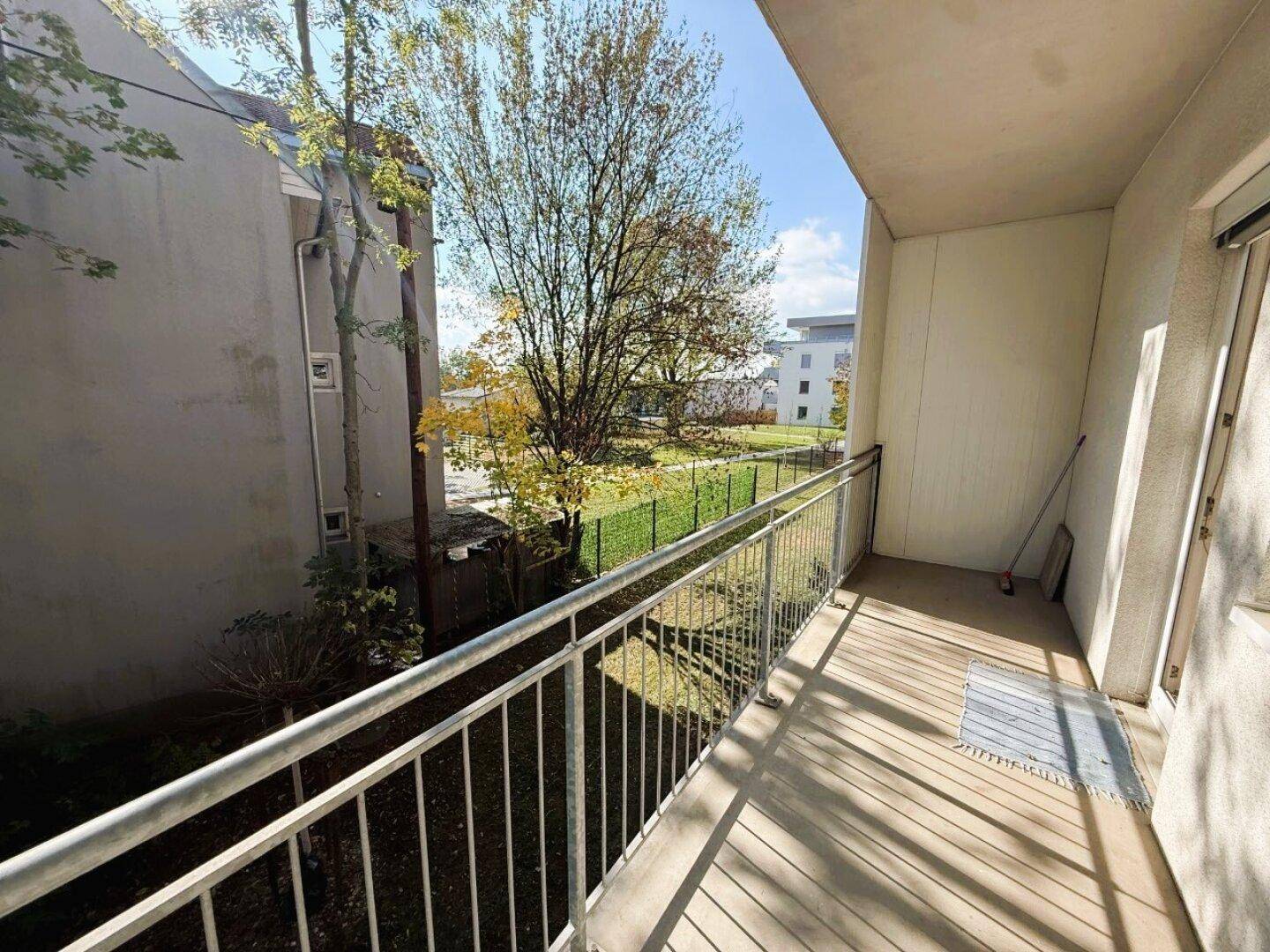 Balkon mit Metallgeländer und Blick auf eine grüne Außenanlage mit Bäumen.