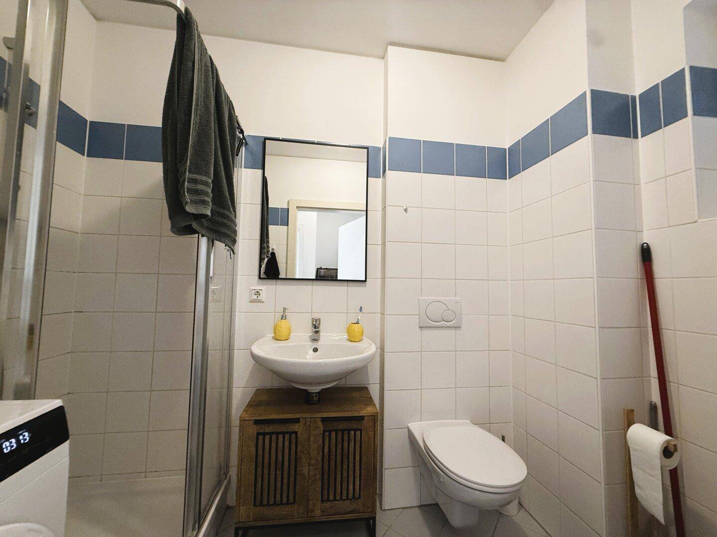 Badezimmer mit weißen und blauen Fliesen, Waschbecken, Toilette und Duschkabine.